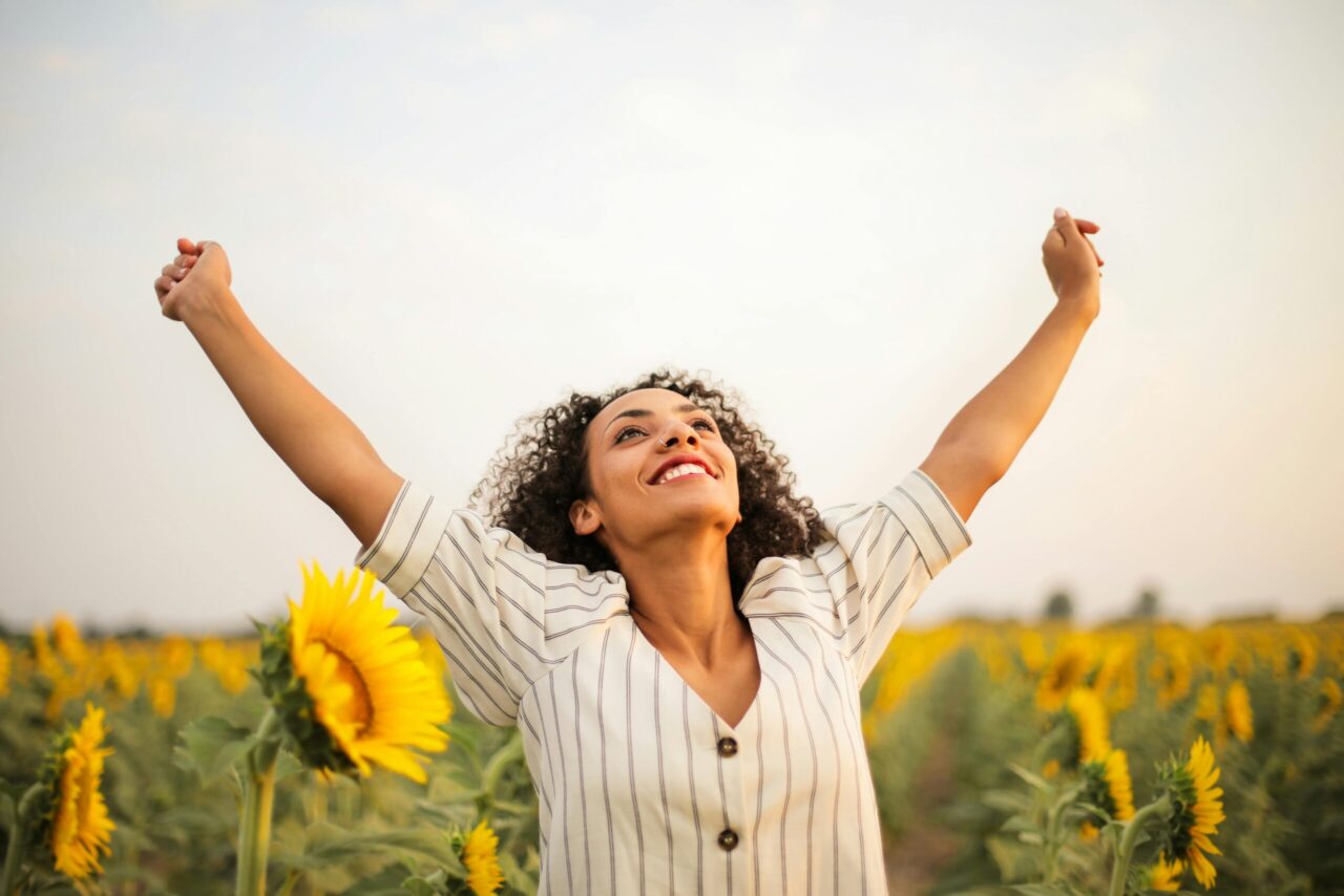 Smiling woman in field of flowers with hands up in the air